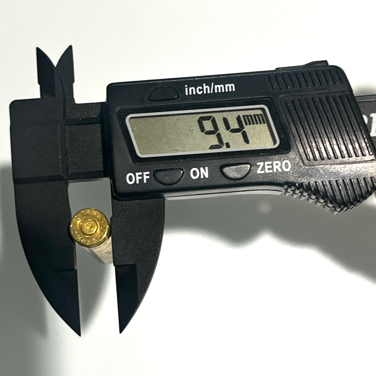 Digital caliper measuring a dirty realistic  .223 brass dummy round casing base, reading 9.4mm