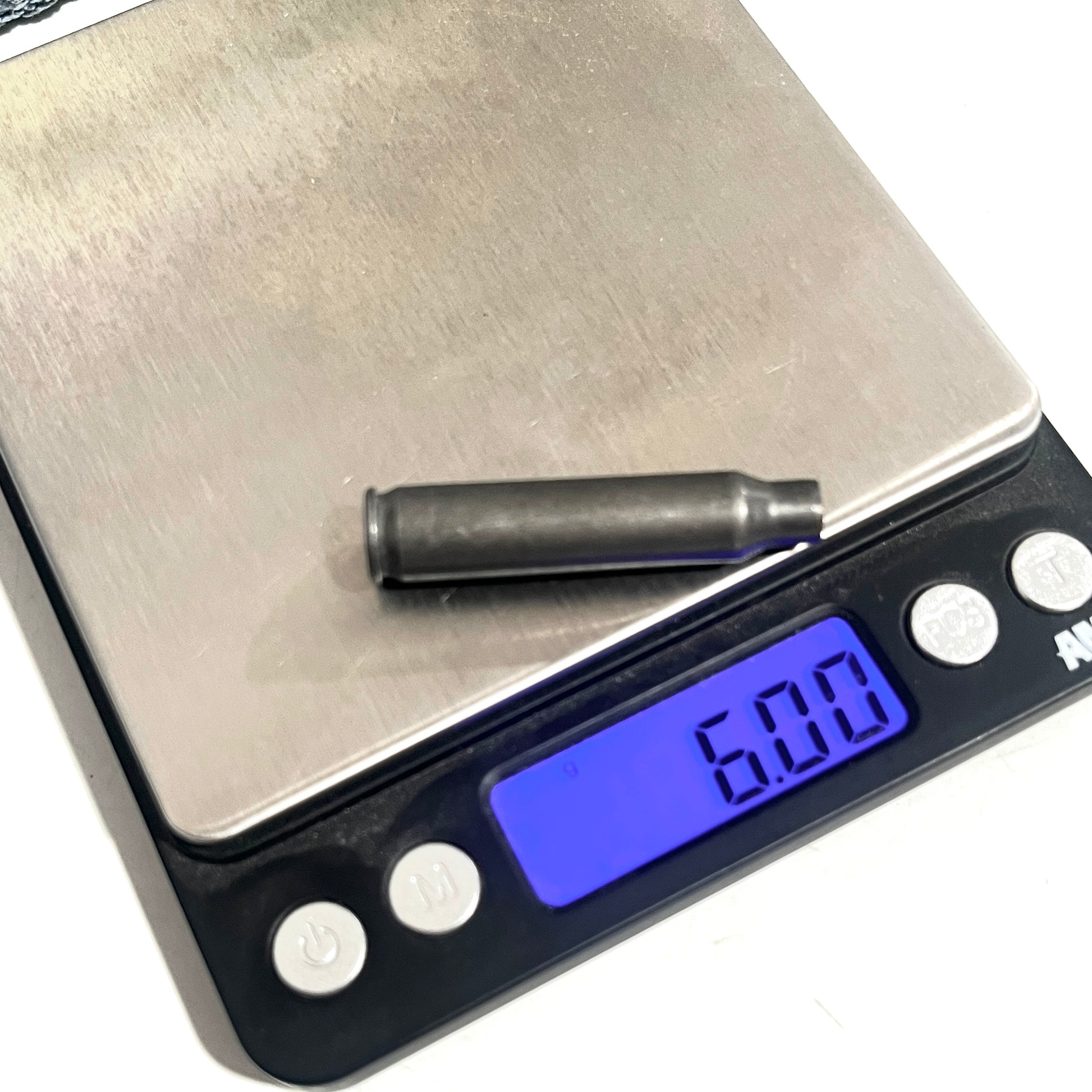 A used gray steel 223 casing rests on a digital scale, which displays a weight of 6.00 grams.