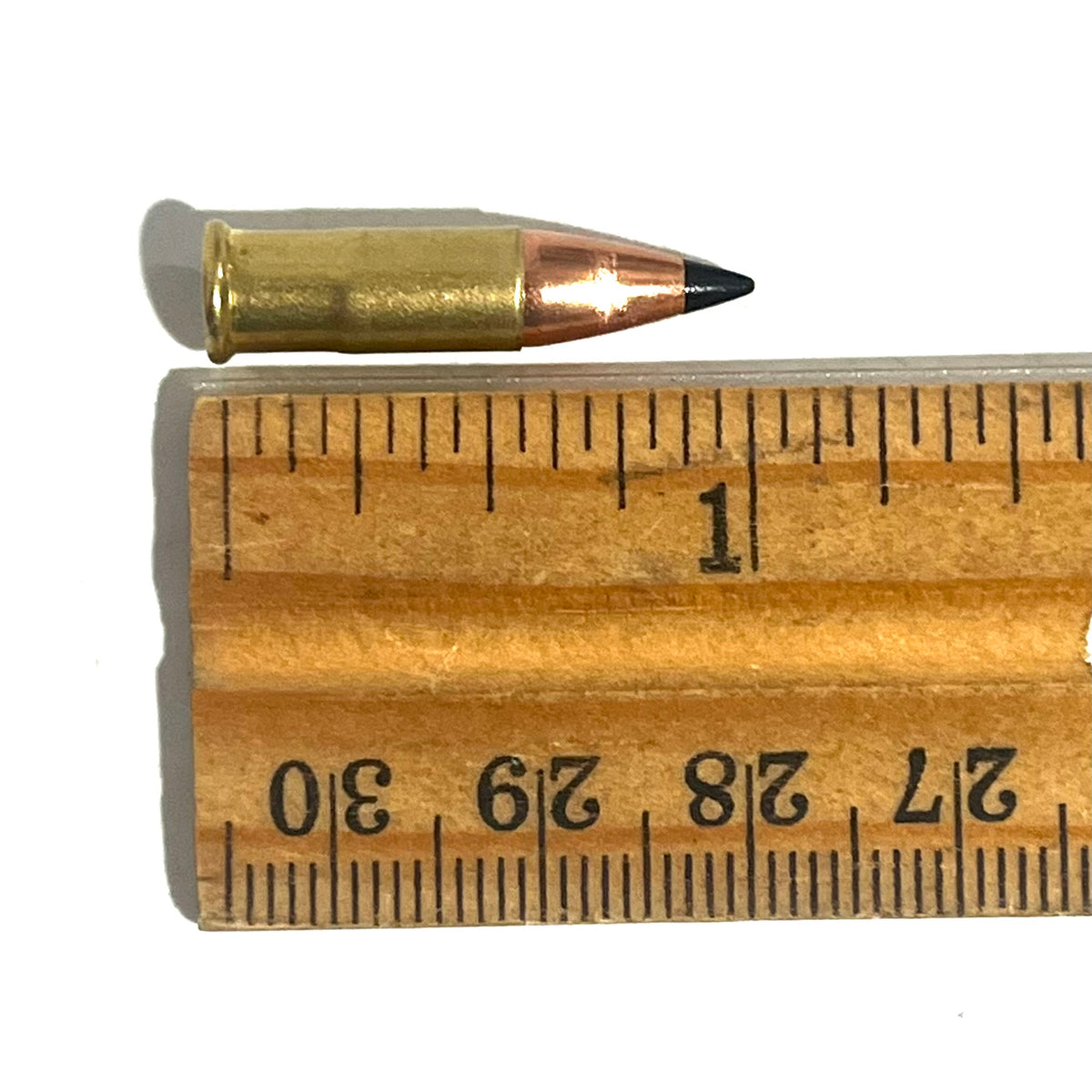 .22 caliber dummy round with a black polymer bullet tip measured on a wooden ruler at approximately 1.1 inches