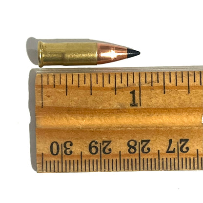 .22 caliber dummy round with a black polymer bullet tip measured on a wooden ruler at approximately 1.1 inches