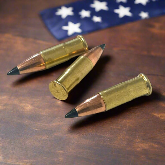 3 .22 caliber dummy rounds with black polymer bullet tips, lying on a wooden table in front of a folded American flag