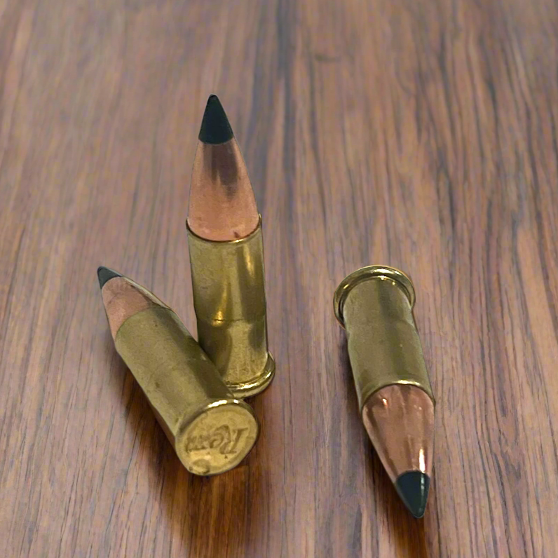 3 .22 caliber dummy rounds with black polymer bullet tips on a wood surface, one showing a Remington headstamp