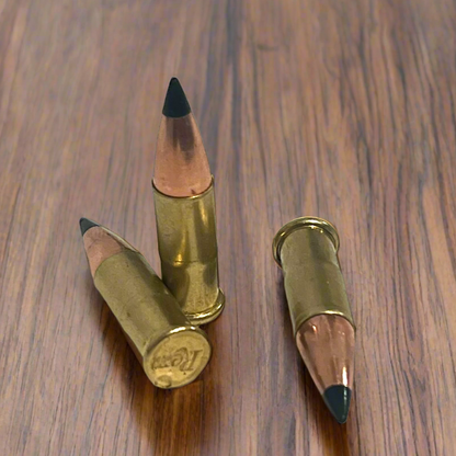 3 .22 caliber dummy rounds with black polymer bullet tips on a wood surface, one showing a Remington headstamp