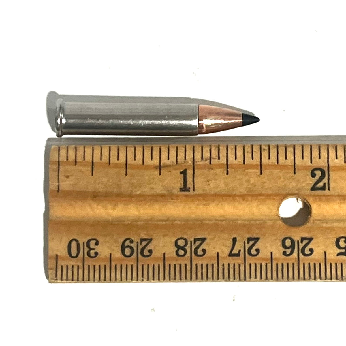 Single .22 Magnum nickel dummy round with black polymer tip laid against a wooden ruler measuring about 1.4 inches