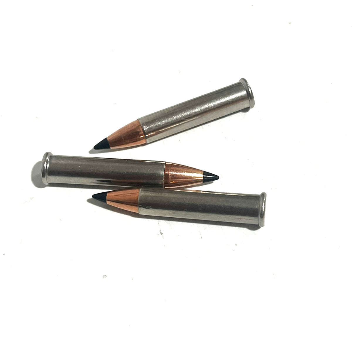 3 .22 Magnum nickel dummy rounds with black polymer tipped bullets laid diagonally on white background