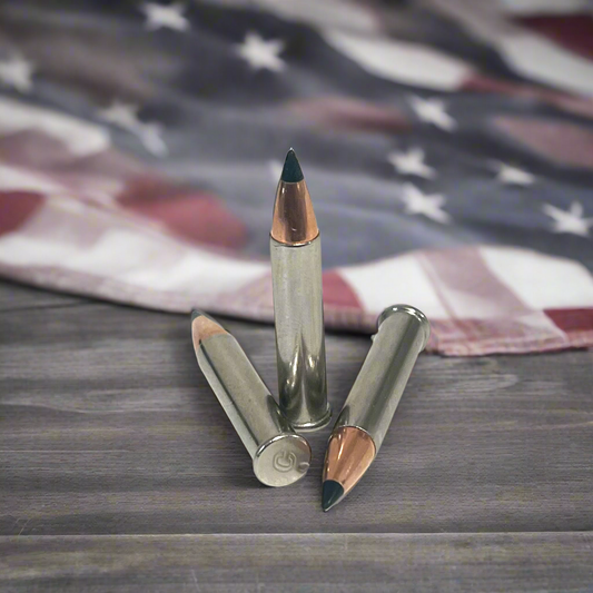 3 .22 Magnum nickel dummy rounds with black polymer tipped bullets, standing and laid on weathered wood in front of blurred American flag
