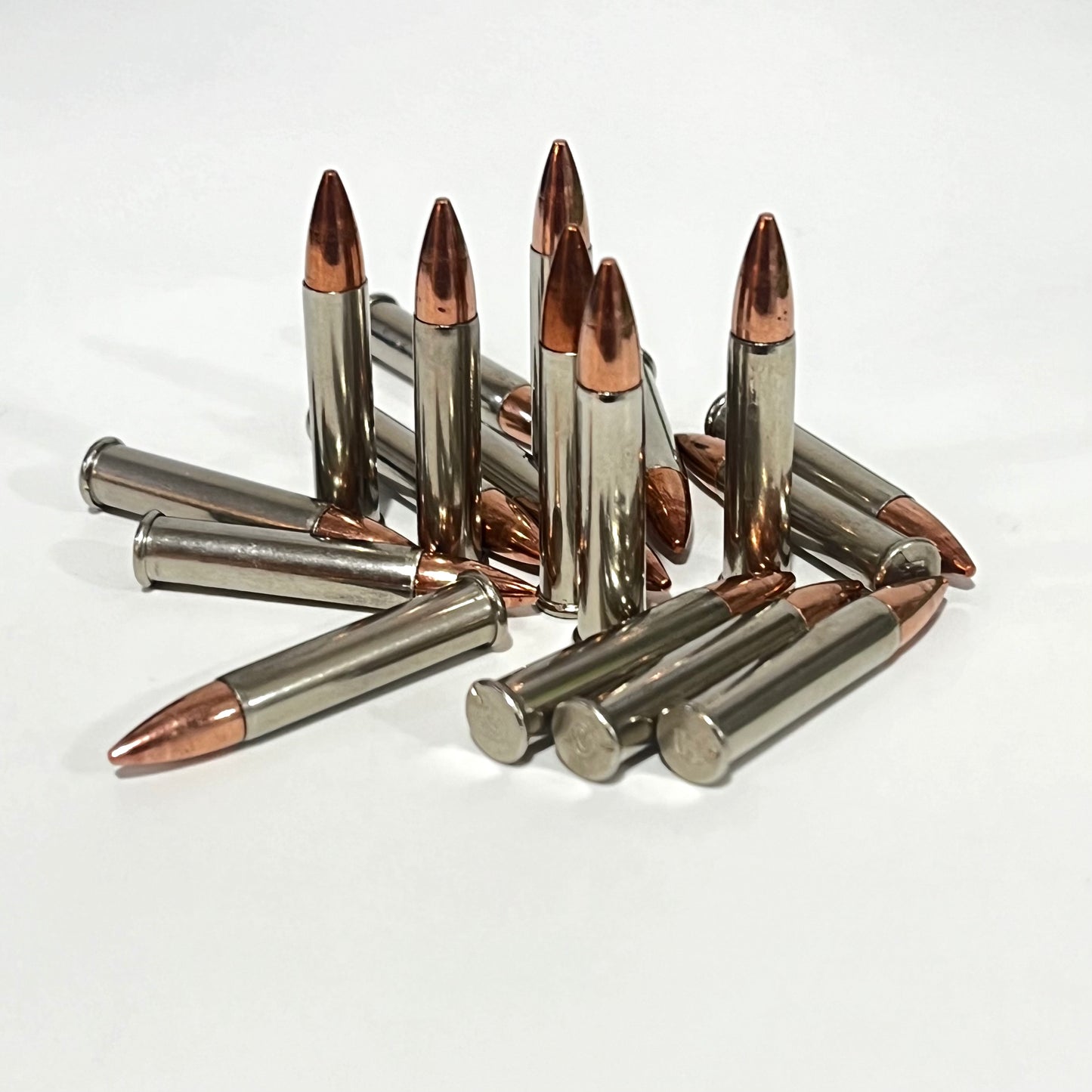 Pile of .22 Magnum nickel dummy rounds with copper bullets scattered on white background