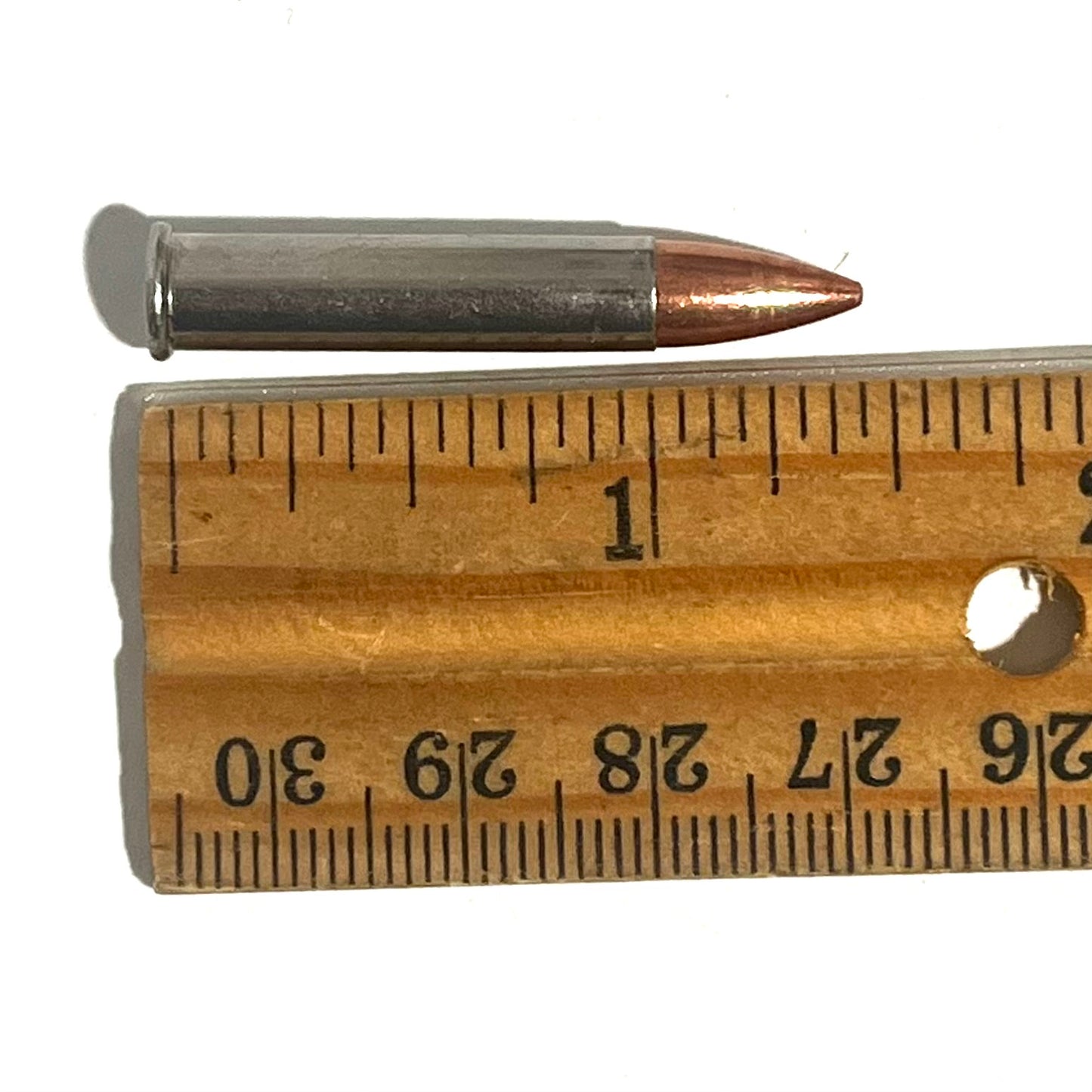 Single .22 Magnum nickel dummy round with copper bullet laid against a wooden ruler measuring about 1.4 inches