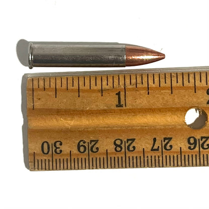 Single .22 Magnum nickel dummy round with copper bullet laid against a wooden ruler measuring about 1.4 inches