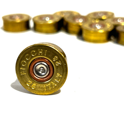 Close-up of a gold brass 28 gauge Fiocchi headstamp with spent primer in focus and blurred shells in the background.