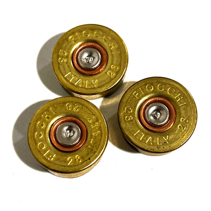 Three gold brass 28 gauge Fiocchi shotgun shell headstamps arranged in a cluster showing stamped text and spent primers.