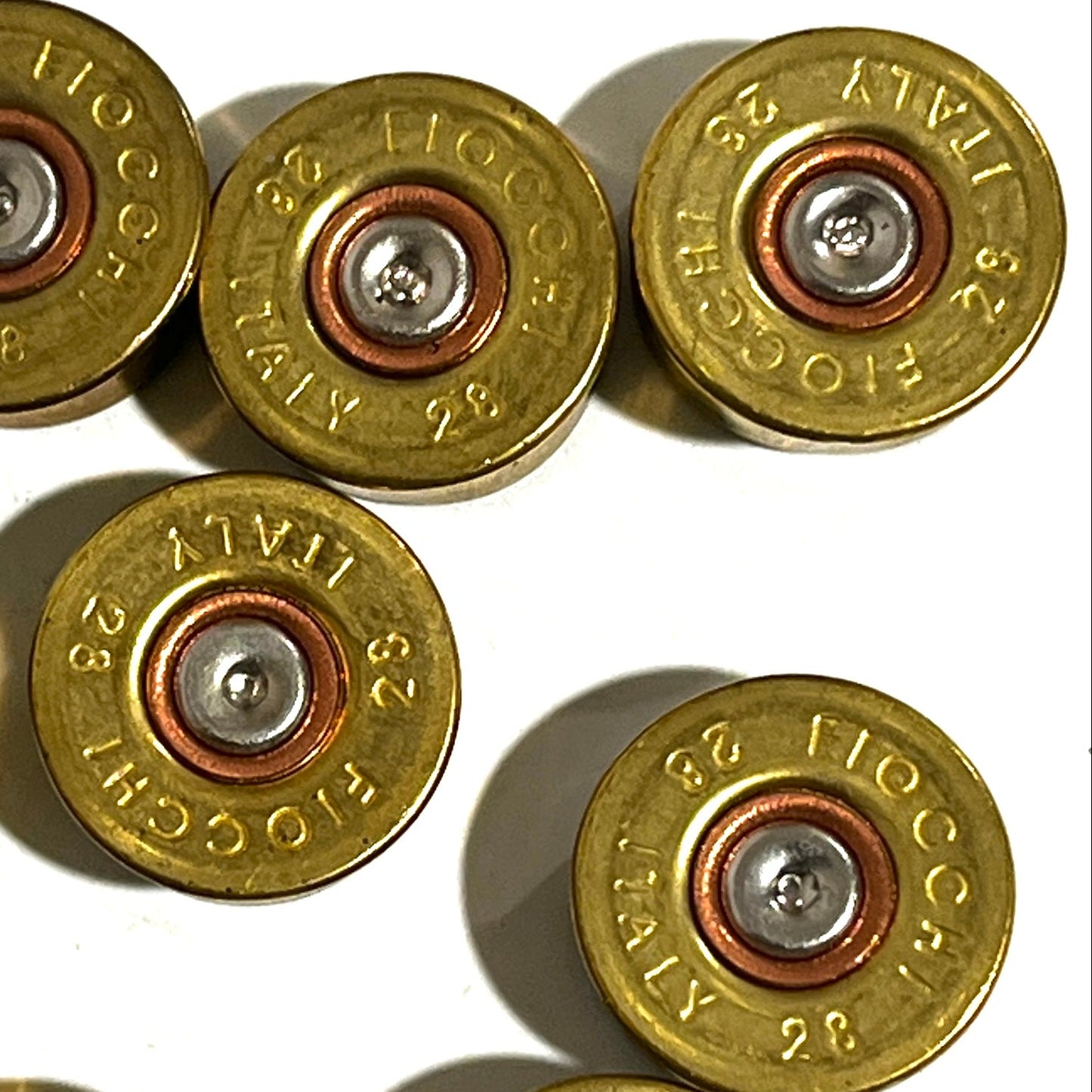Macro view of six gold brass 28 gauge Fiocchi shotgun shell headstamps showing stamped text and spent primers.