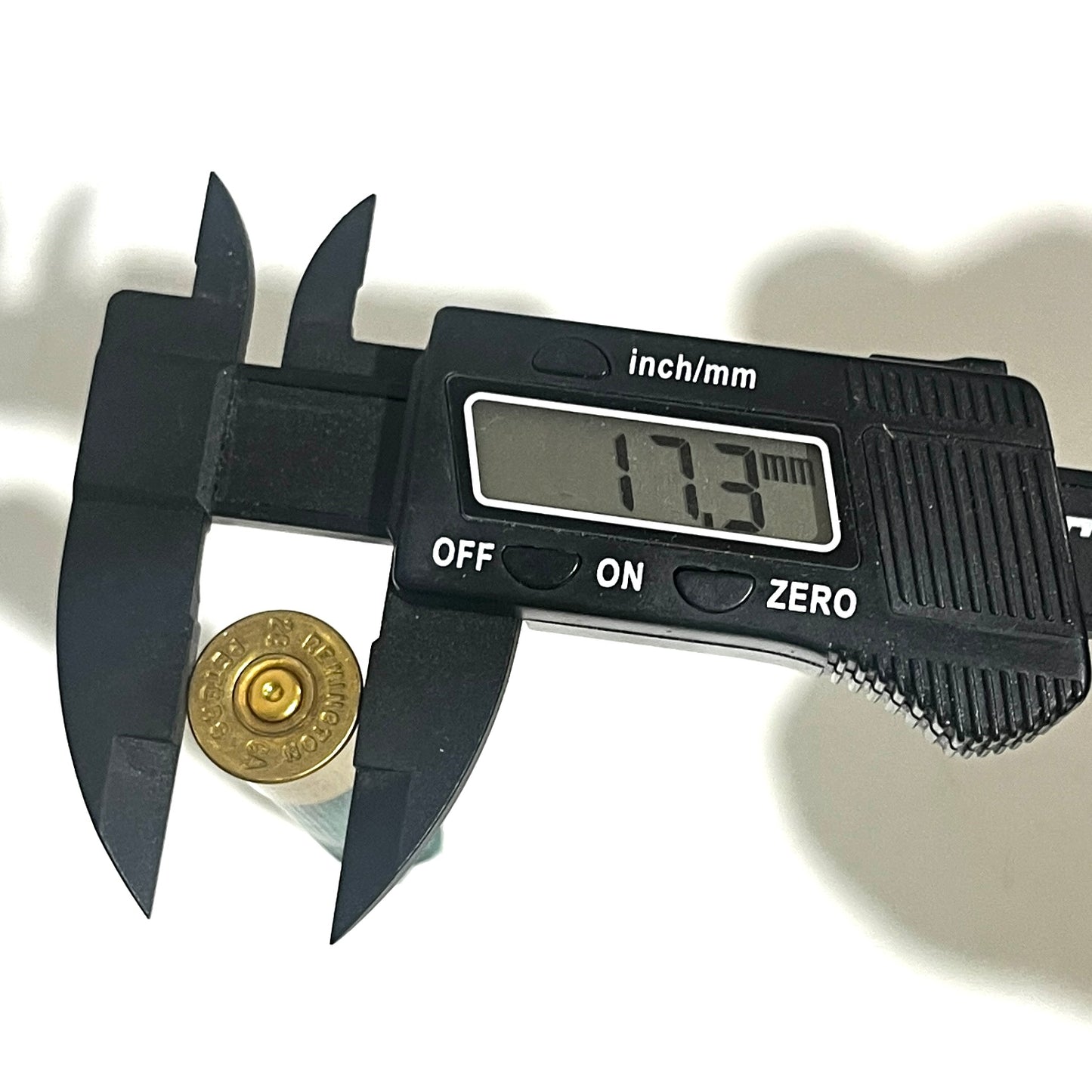 A black digital caliper measuring the brass base diameter of a 28 gauge shotgun hull, reading 17.3 mm.