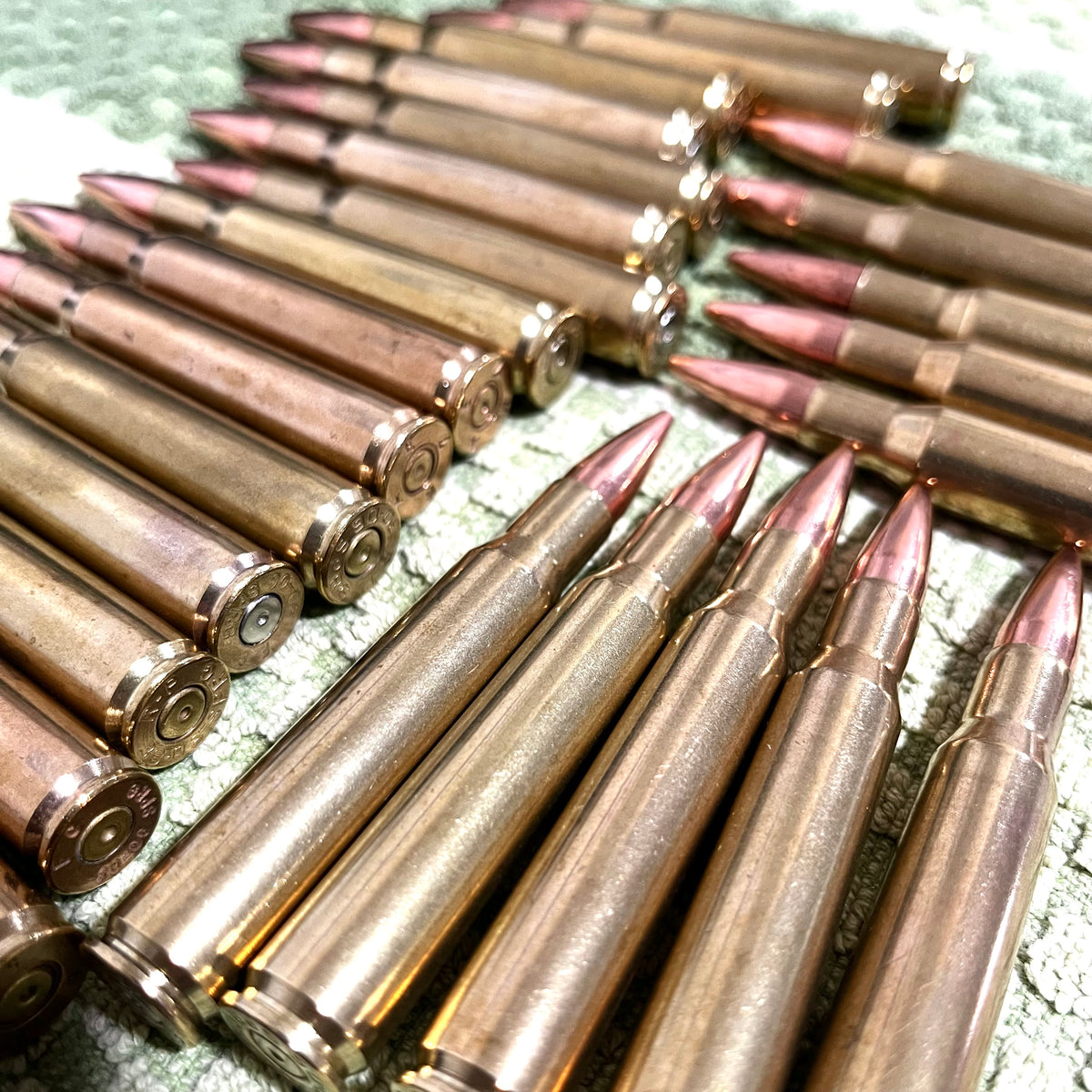 Multiple rows of 30-06 dummy rifle rounds with brass cases and new bullets arranged in a fan pattern