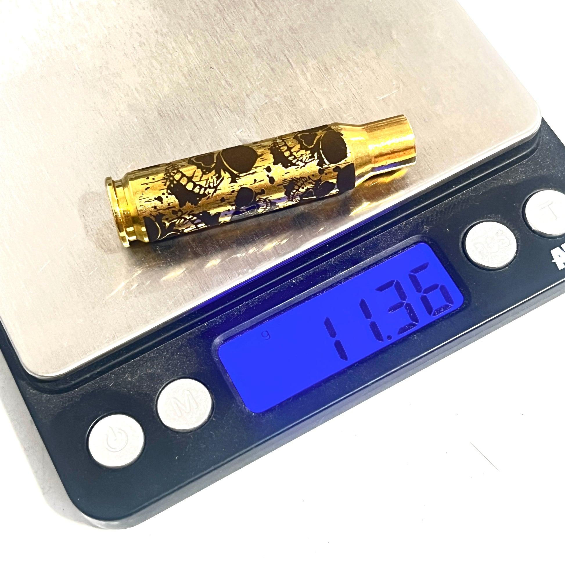 Single laser-engraved skull 308 WIN brass case resting on a digital scale displaying a weight of 11.36 grams.