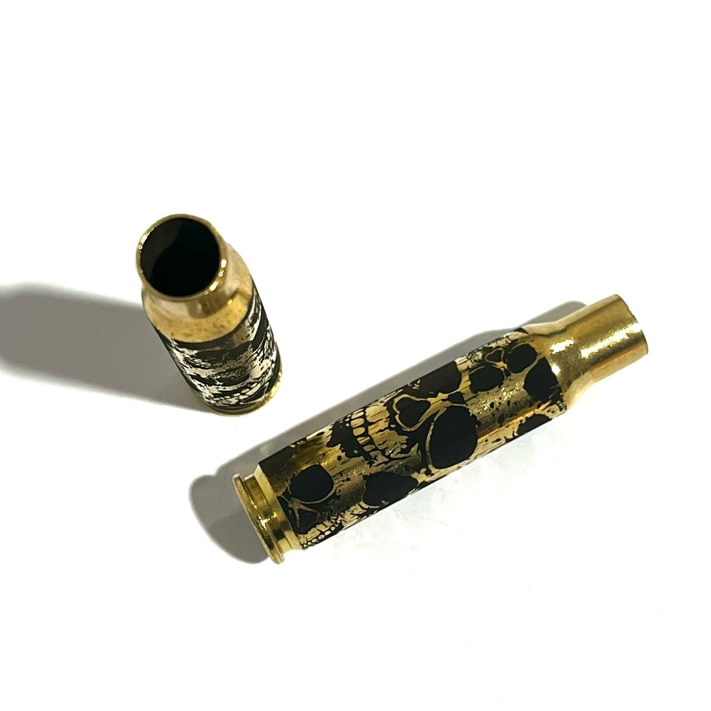 Two 308 WIN brass shells with laser-engraved skulls, one standing upright and one lying flat.
