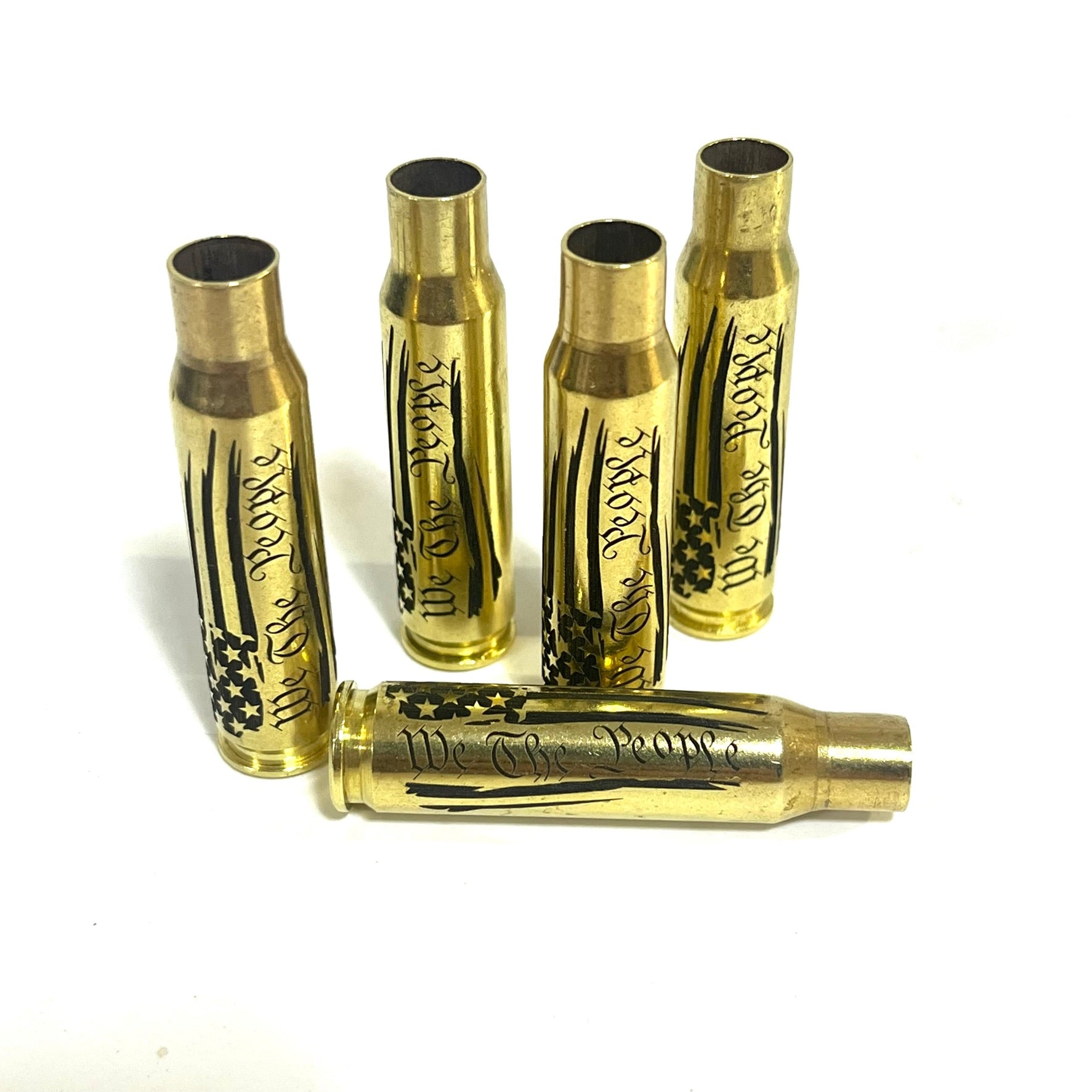 Four upright and one horizontal .308 WIN cartridge cases engraved with a We The People flag design on a white surface.