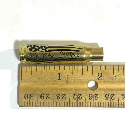 One horizontal .308 WIN empty cartridge measured next to a wooden ruler, showing a length of just over 2 inches.