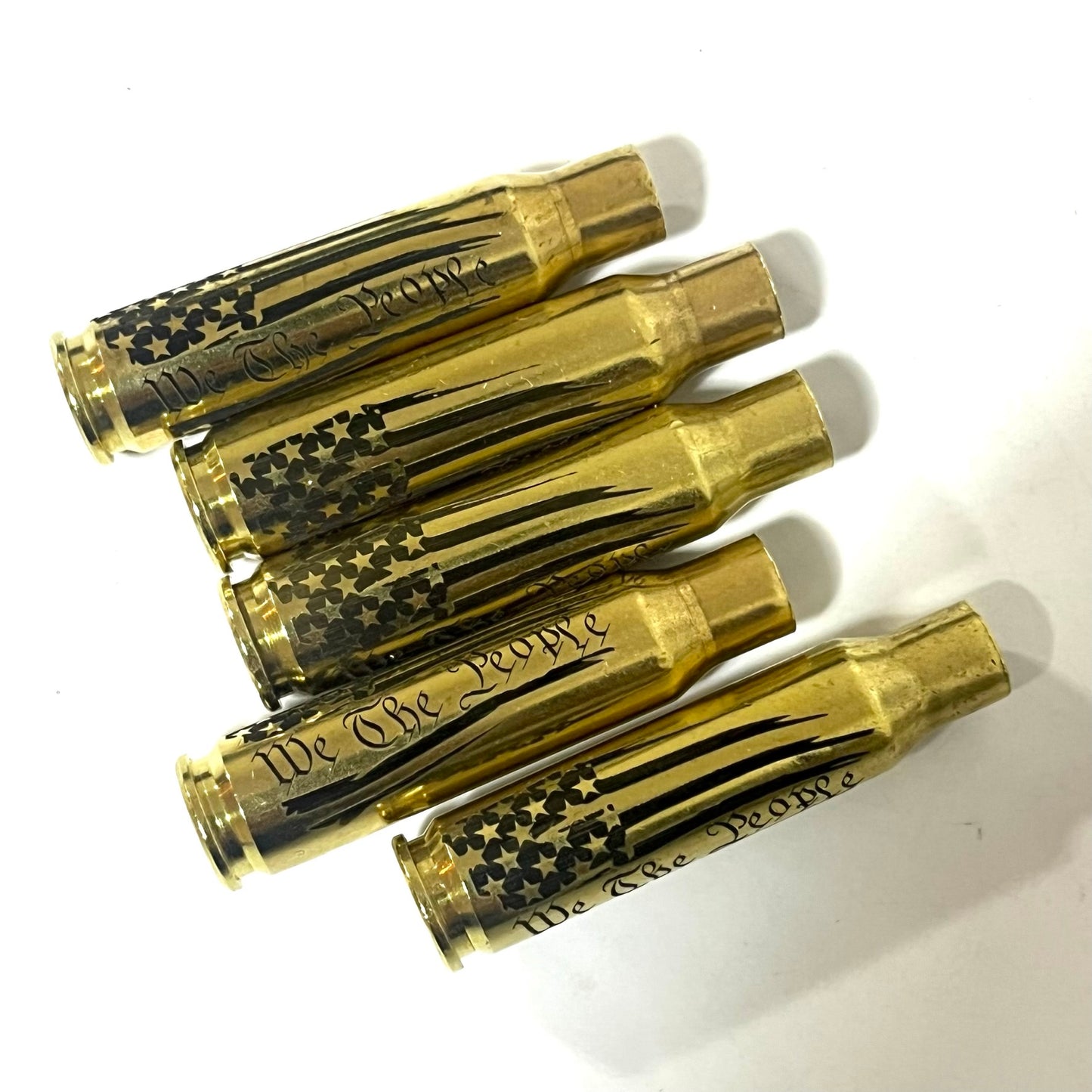 5 horizontal .308 WIN empty cartridge cases engraved with the We The People flag design on a clean white surface.