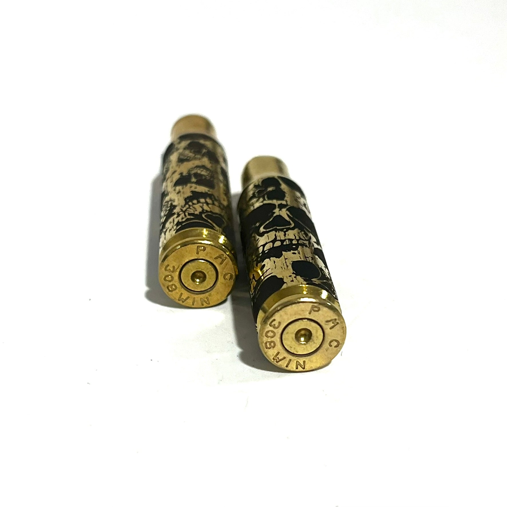 Two 308 WIN brass casing bases showing headstamps and laser-etched skull graphics.