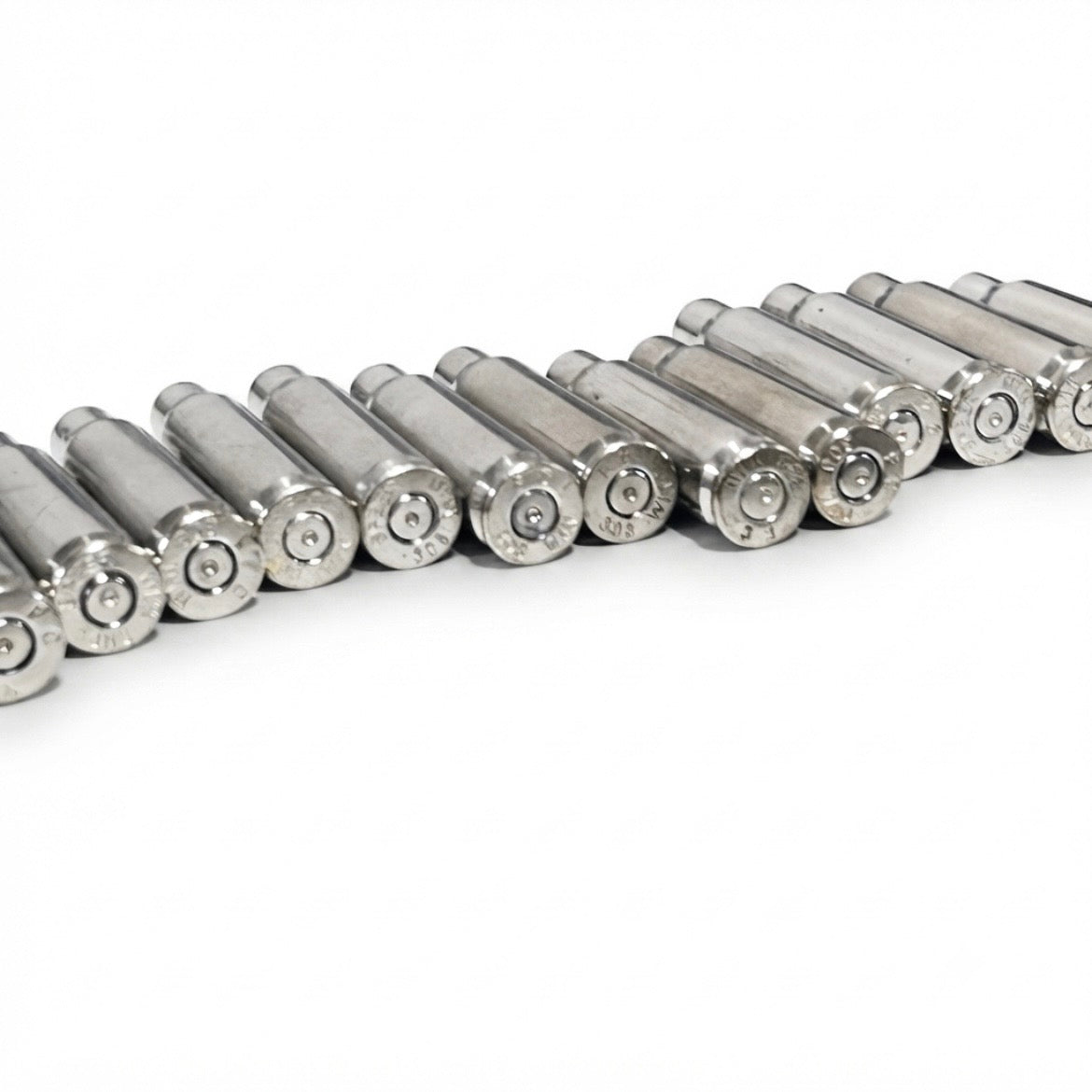 Diagonal row of eleven empty silver-tone .308 nickel brass lying flat on a white surface, bases facing the camera.