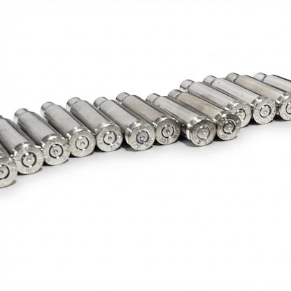 Diagonal row of eleven empty silver-tone .308 nickel brass lying flat on a white surface, bases facing the camera.