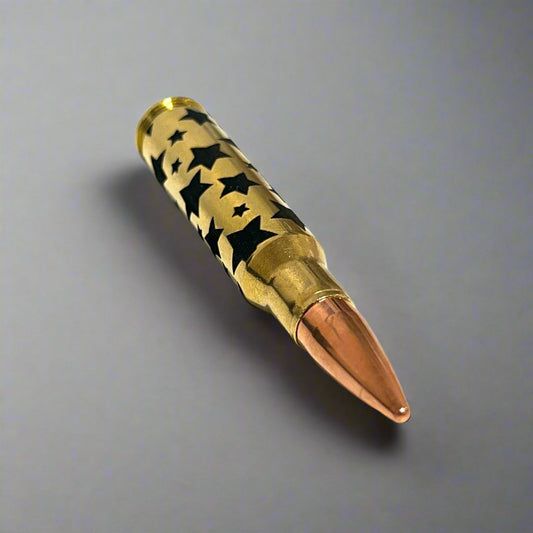 Brass rifle cartridge with black star pattern and copper bullet tip lying at an angle on a gray background