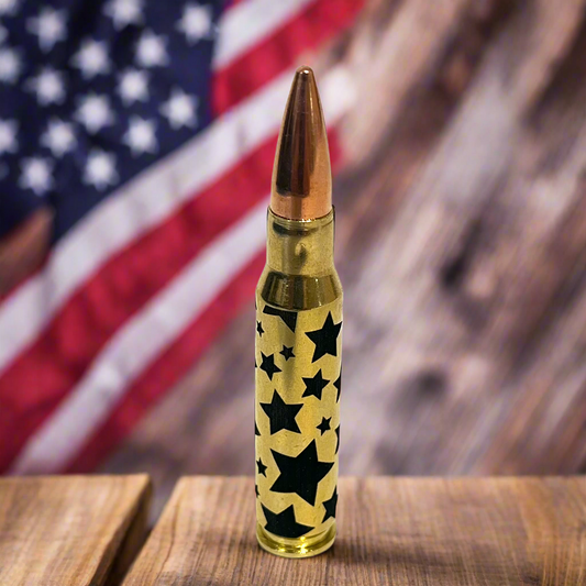Brass rifle cartridge with black star pattern and copper bullet tip standing upright in front of an American flag background