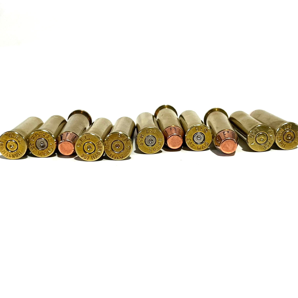 Row of 10 empty brass cases and flat-nose dummy rounds with mixed headstamps lined up on a white background
