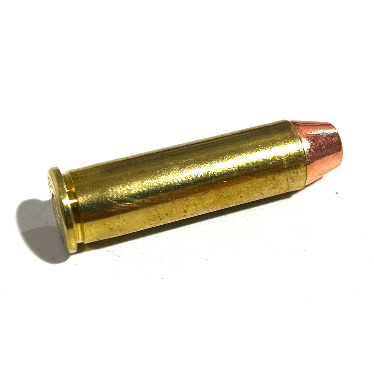 Single 357 Magnum brass dummy round for film props lying at an angle on a white background showing the brass case and flat-nose bullet