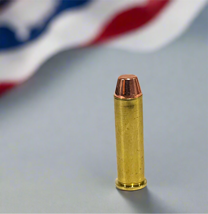 Single 357 Magnum brass dummy round with flat-nose bullet standing upright against a blurred American flag background