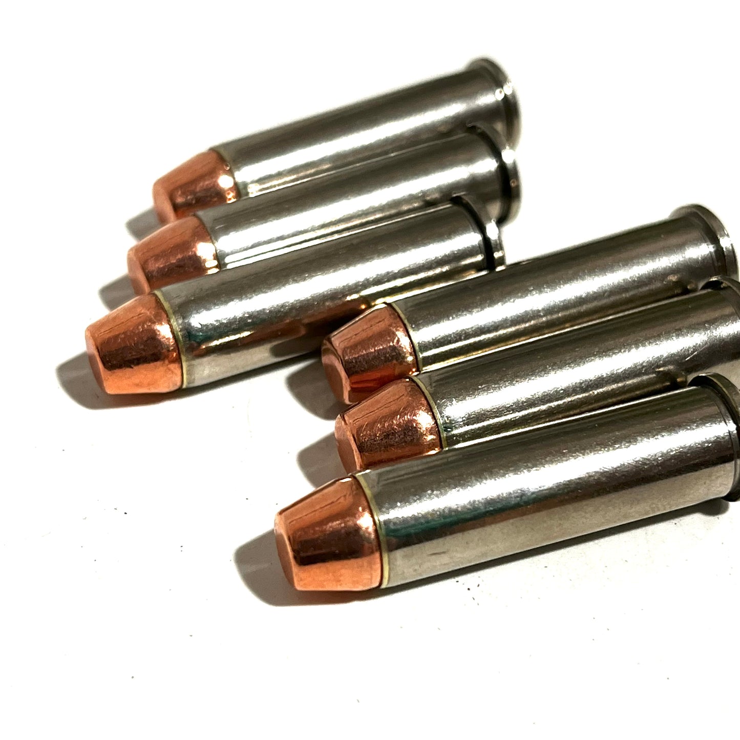 Five nickel dummy rounds with copper flat nose bullets arranged diagonally in a row on a plain white surface.