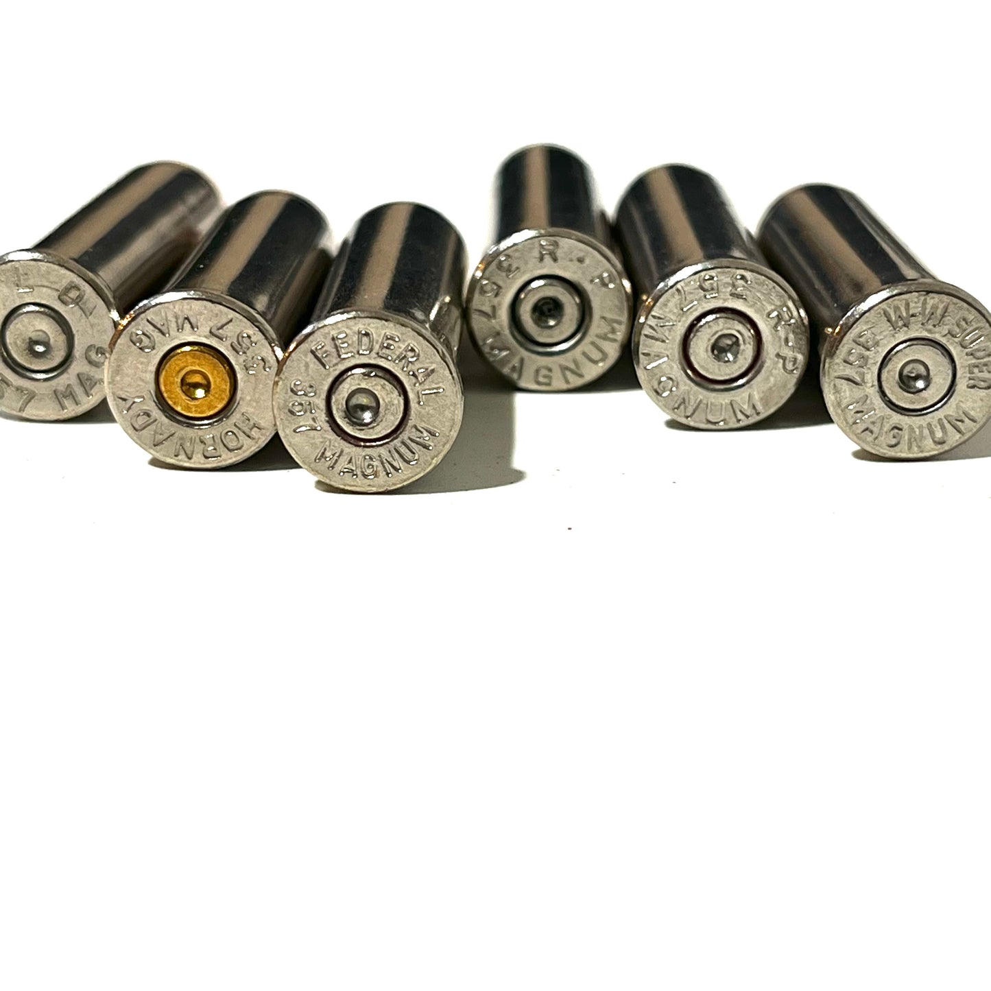 A row of various nickel inert casings showing different headstamps and spent primers including Federal, Hornady, and W-W Super 357 Magnum.