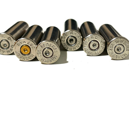 A row of various nickel inert casings showing different headstamps and spent primers including Federal, Hornady, and W-W Super 357 Magnum.