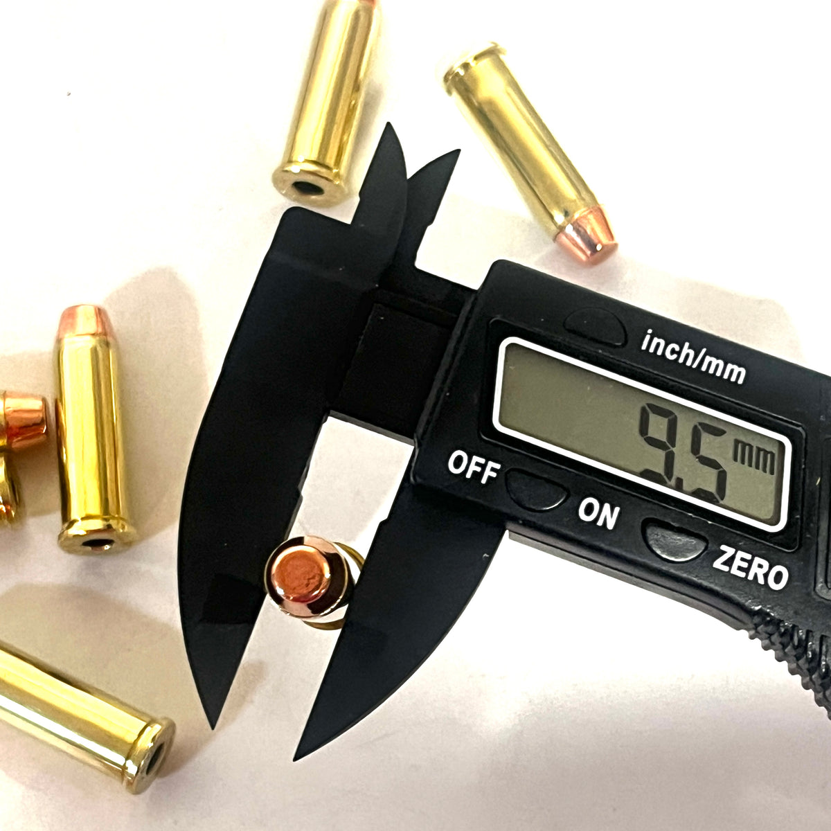 Digital caliper measuring a 38 Special flat nose bullet's diameter at 9.5 millimeters, with brass cases scattered nearby