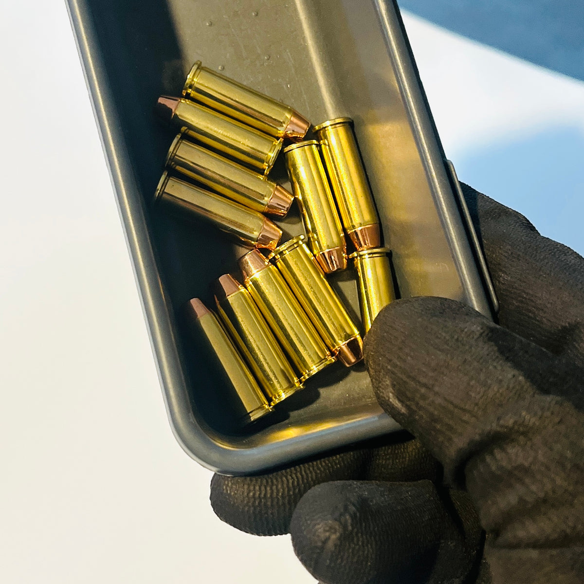 Gloved hand holding a gray metal tray of 11 once-fired brass 38 Special cartridges fitted with copper bullets and spent primers