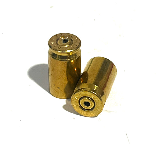 2 gold .380 caliber brass shell casings standing on a white background, one with a visible drilled hole in the primer pocket