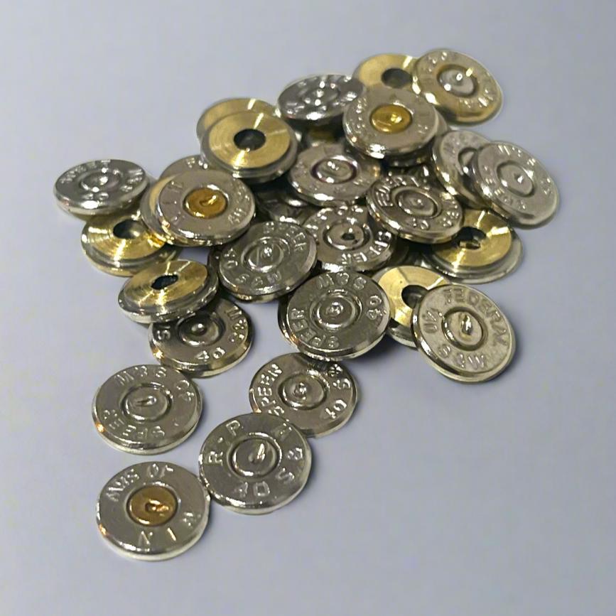 A scattered pile of polished 40 S&W nickel bullet slices on a light grey background, featuring mixed legible headstamps like SPEER and FEDERAL with intact spent brass primers. 