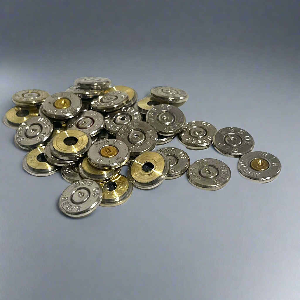 A scattered pile of polished 40 S&W nickel bullet slices with intact spent primers on a light grey background.