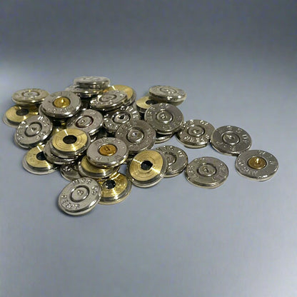 A scattered pile of polished 40 S&W nickel bullet slices with intact spent primers on a light grey background.