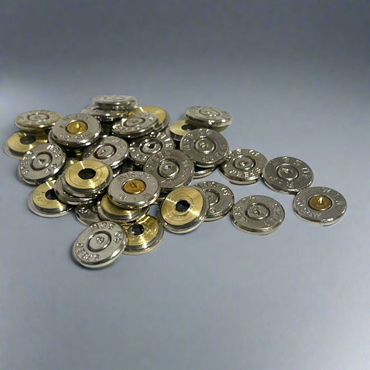 A scattered pile of polished 40 S&W nickel bullet slices with intact spent primers on a light grey background.