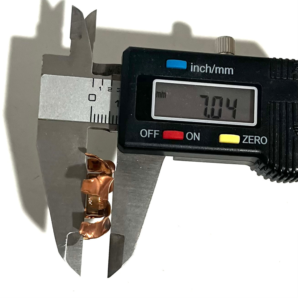 Digital caliper measuring the height of an expanded copper bullet jacket blossom at 7.04 mm