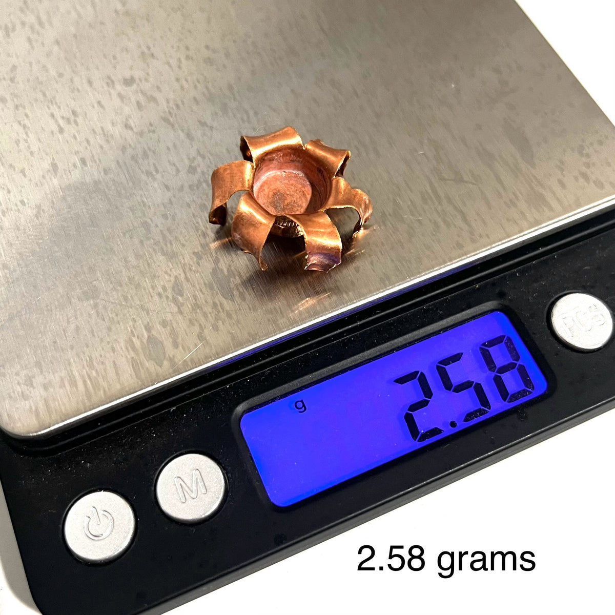 An expanded copper bullet jacket blossom on a digital scale reading 2.58 grams