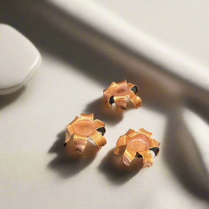 Three expanded copper bullet jacket blossoms resting on a light surface in soft shadow