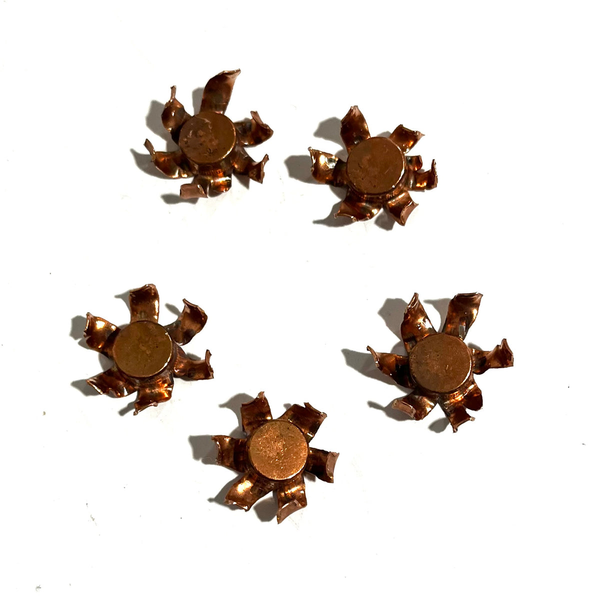 Five expanded copper bullet jacket blossoms each with a flattened lead core visible, scattered on white background