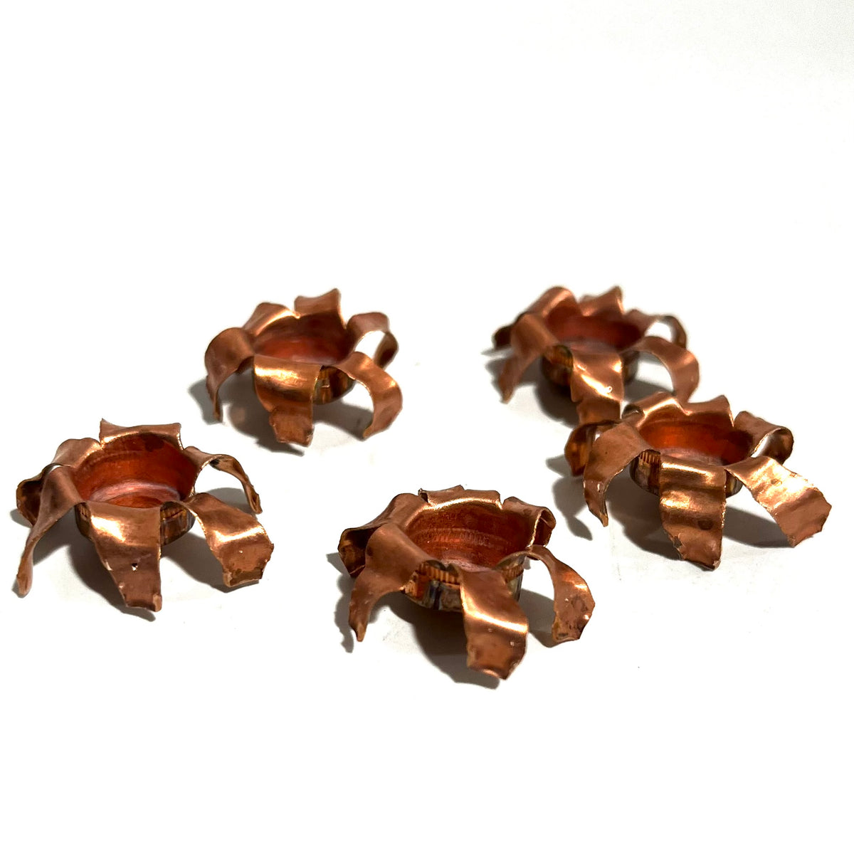 Five expanded copper bullet jacket blossoms scattered on white background