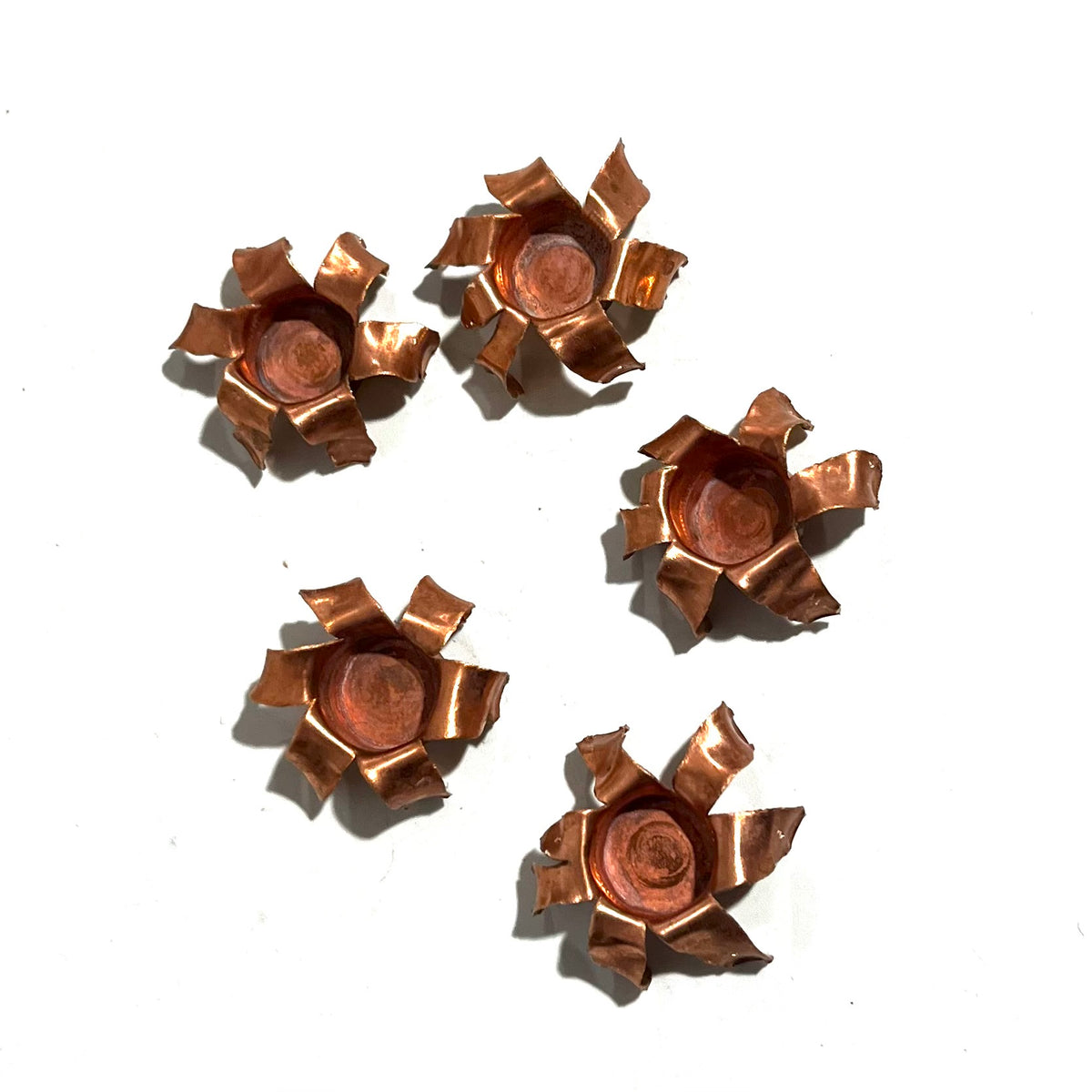Five expanded copper bullet jacket blossoms scattered on white background, viewed from above