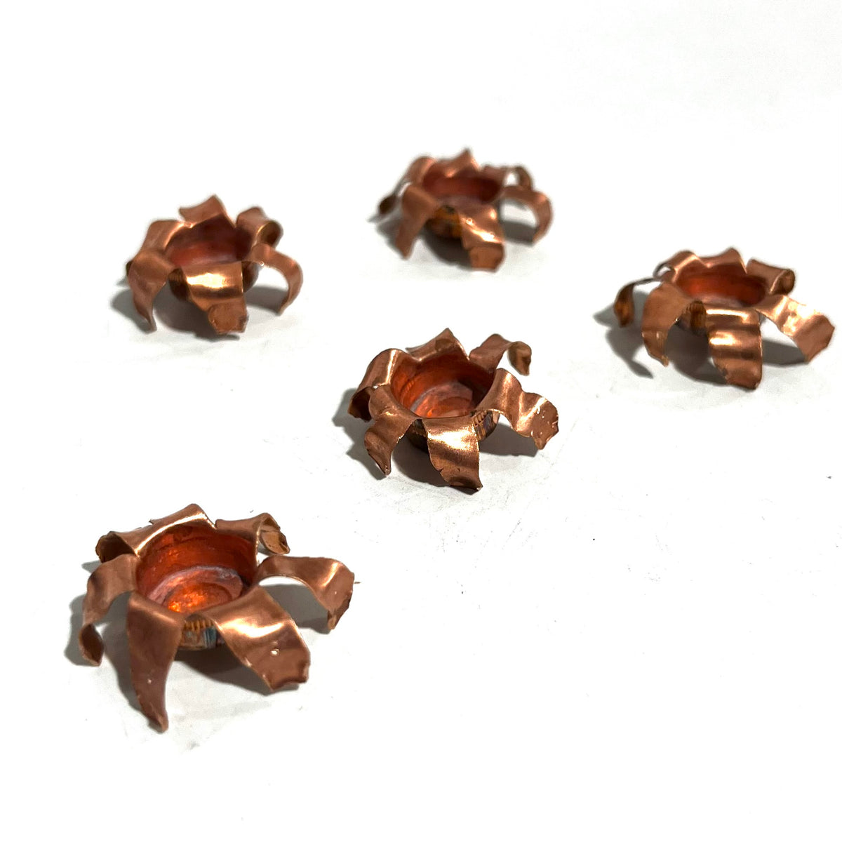 Five expanded copper bullet jacket blossoms scattered on white background