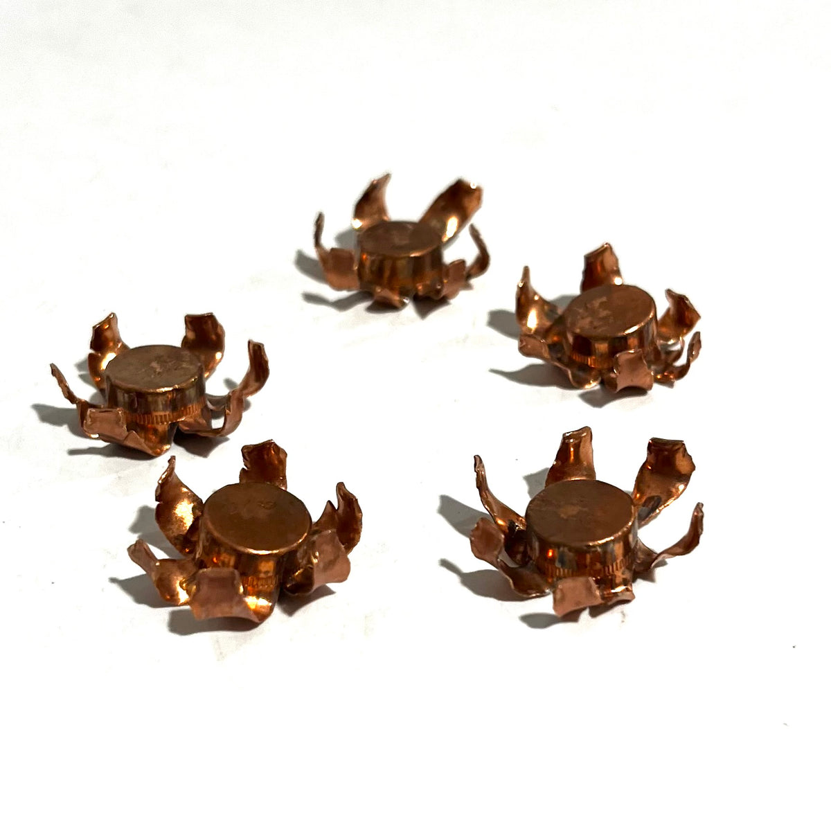 Five expanded copper bullet jacket blossoms each with a flattened lead core visible in the center, scattered on white background