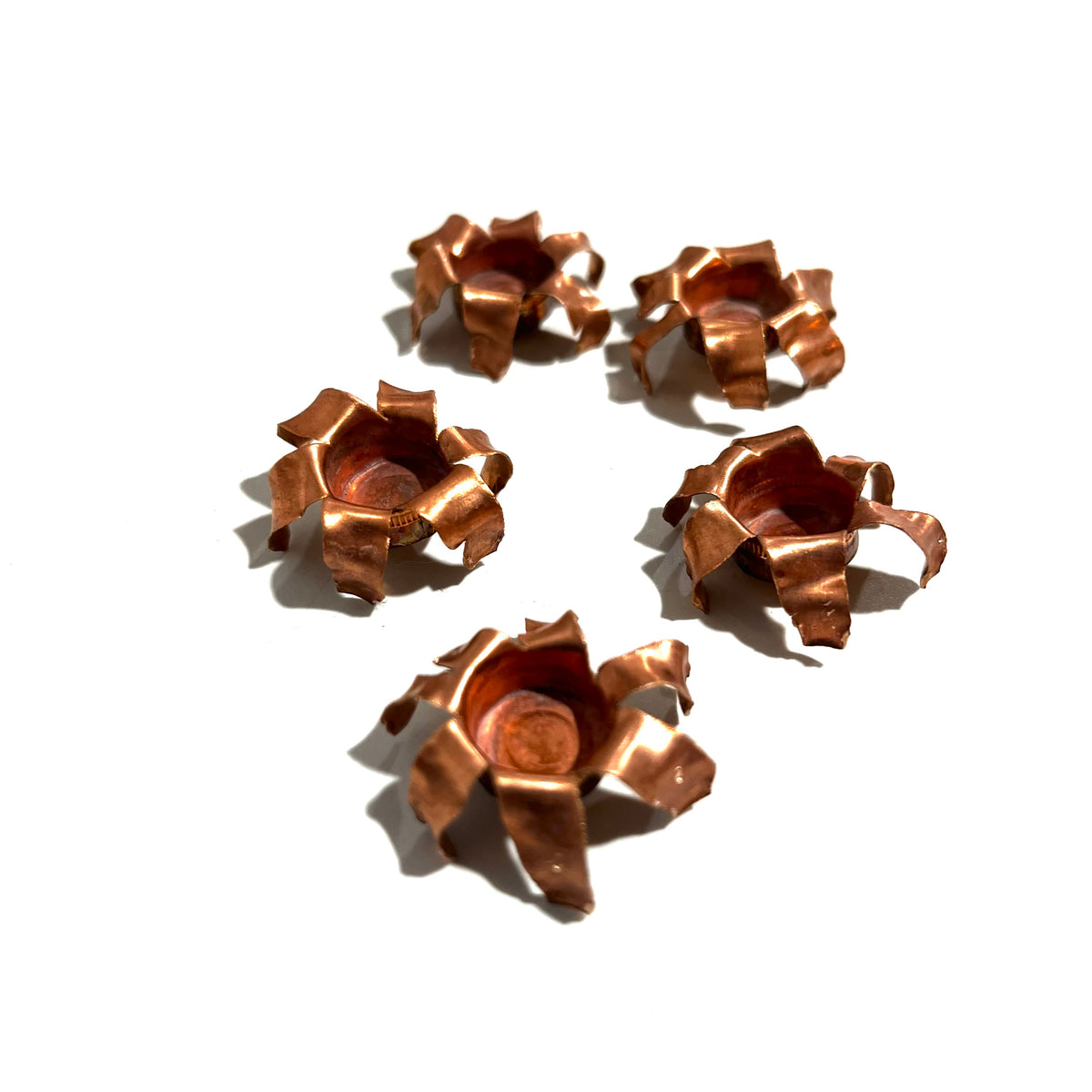 Five expanded copper bullet jacket blossoms scattered on white background, viewed from above